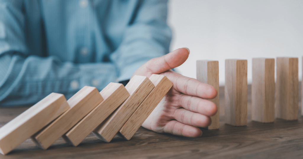 photo of hand stopping a row of collapsing dominos